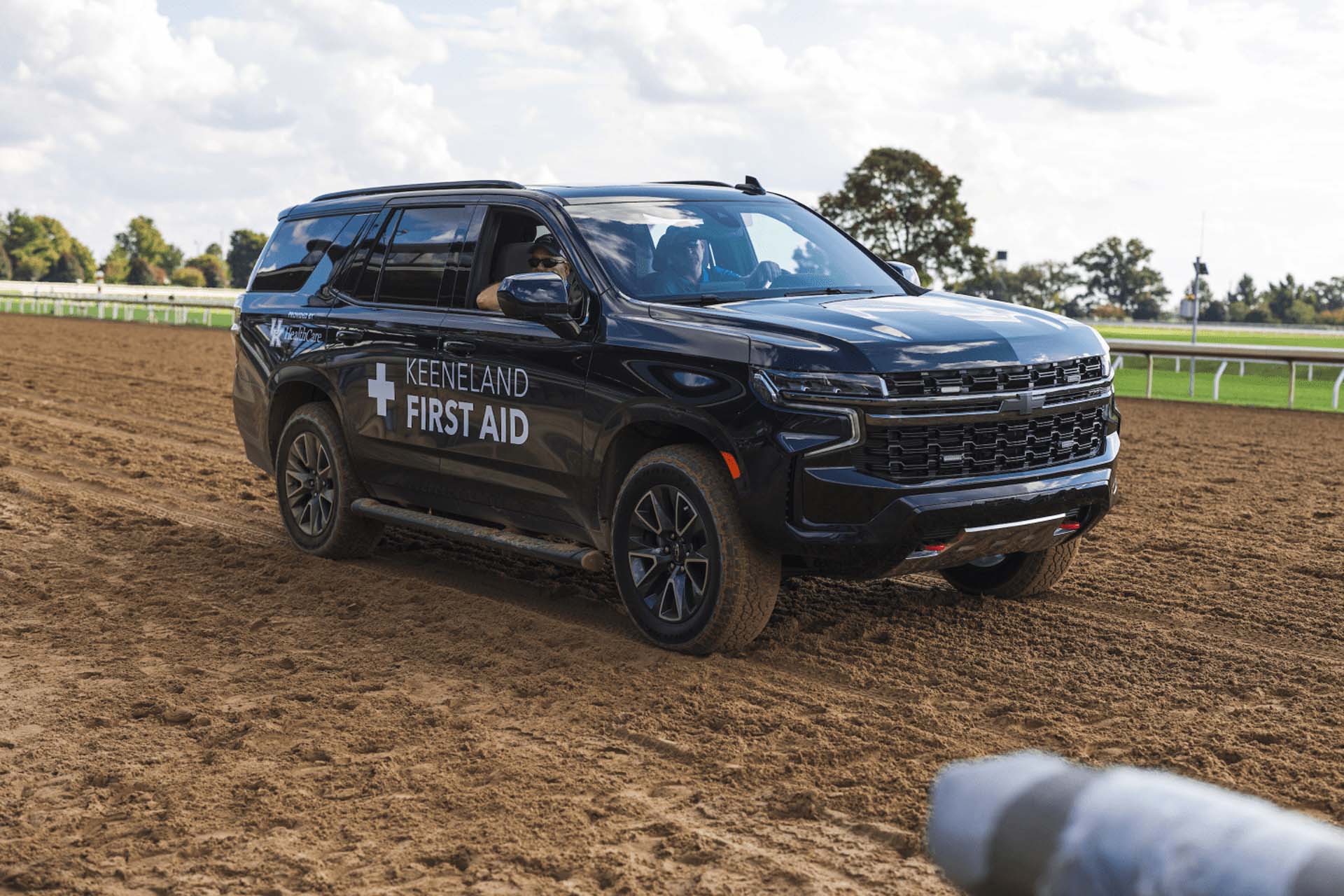 A picture of the Keenriders First Aid car on the dirt track. It is a large black Chevy SUV.